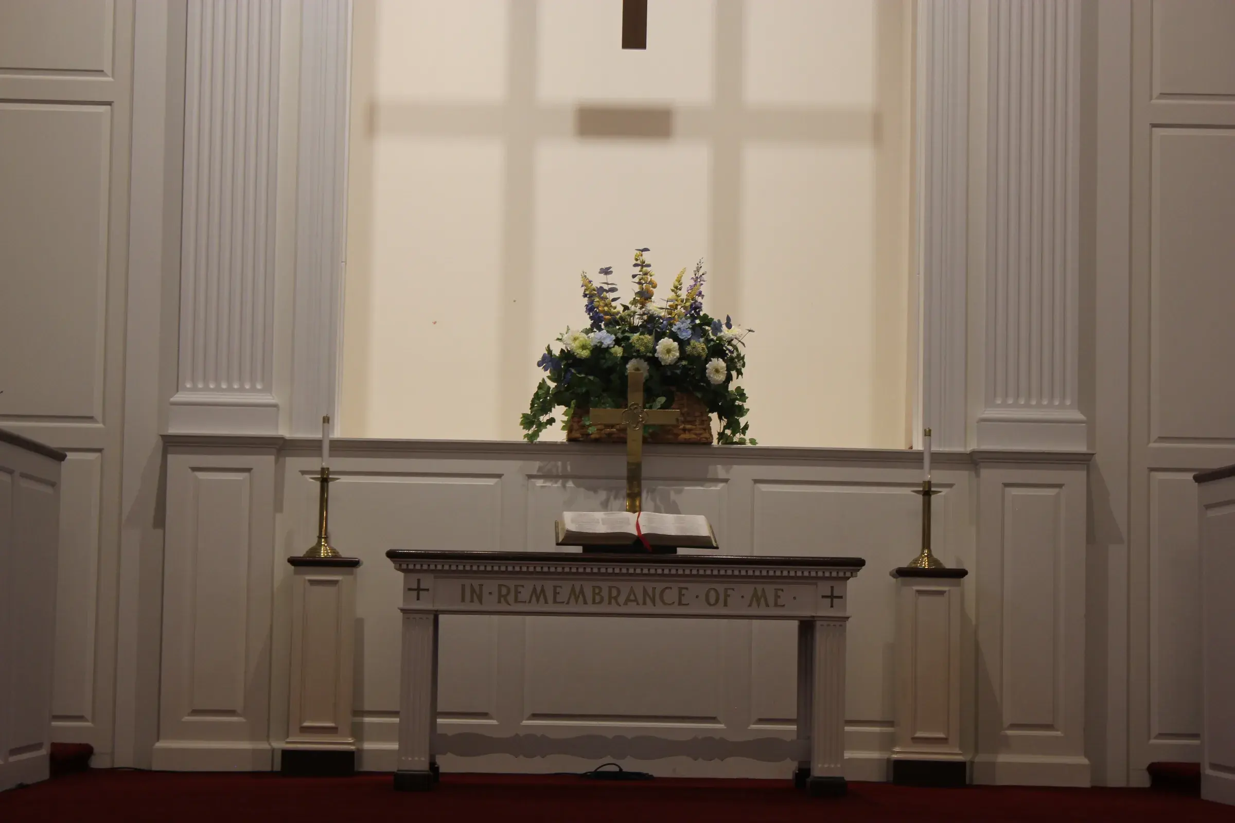 The communion table at Second Baptist Church of Suffield, inscribed 'In Remembrance of Me', set with a cross, open Bible, and flowers